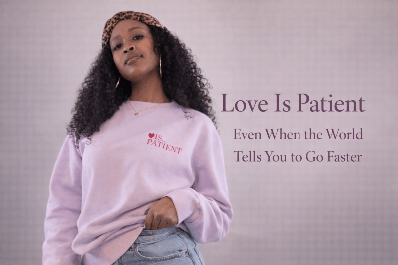 Black woman wearing a lavender “Love Is Patient” sweatshirt, standing confidently against a neutral background, promoting the blog post “Love Is Patient: Even When the World Tells You to Go Faster.