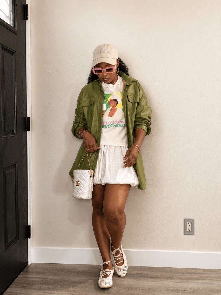 Steffanie Monae wearing an olive jacket, graphic tee, bubble skirt, pink sunglasses, and woven ballet flats