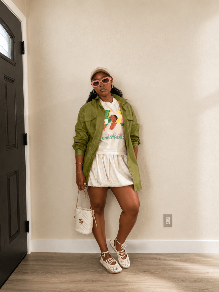Steffanie Monae wearing an olive jacket, graphic tee, bubble skirt, pink sunglasses, and woven ballet flats